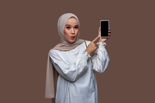 히잡을 쓴 젊은 여성이 놀란 표정으로 휴대폰 화면을 가리키고 있었다