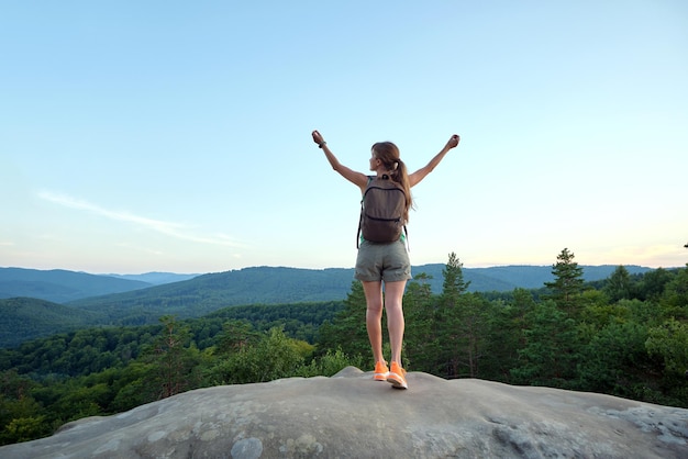 Young woman hiker standing alone with outstretched arms on mountain footpath enjoying view of evening nature on wilderness trail Active way of life concept