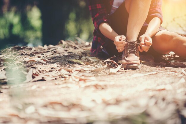 Young woman hiker stops to tie her shoe on a summer hiking trail in forest