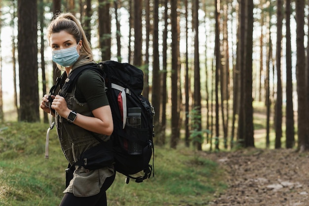 Young woman hiker with a backpack wearing prevention mask during her hike in forest