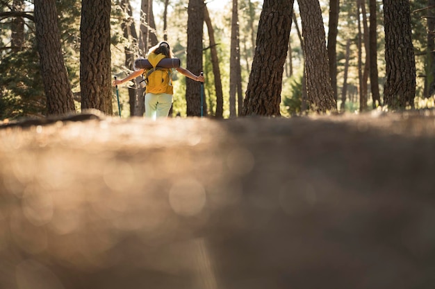 Young woman in hiking clothes and large backpack equipped with trenches and enjoys the freedom of nature with open arms surrounded by a variety of trees