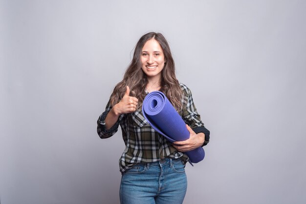 young woman hiolding mat and showing thumb up.