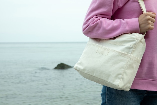 Young woman hold stylish eco bag against sea