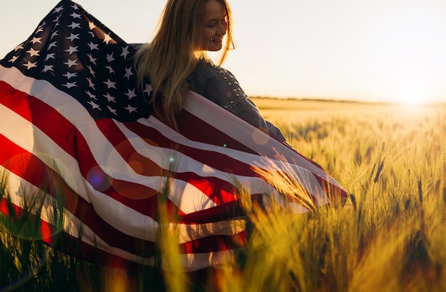 日没時にアメリカの国旗を保持している若い女性