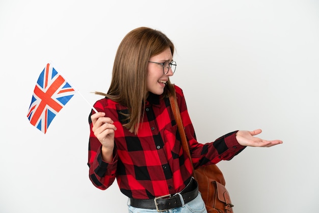 Фото Молодая женщина с флагом соединенного королевства на синем фоне с удивленным выражением лица, глядя в сторону