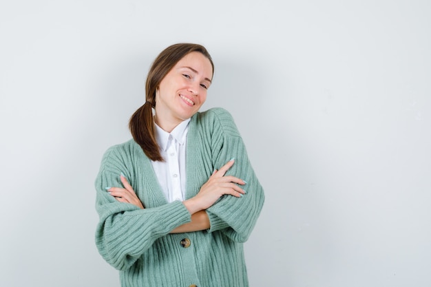 Young woman holding arms folded in blouse, cardigan and looking proud. front view.