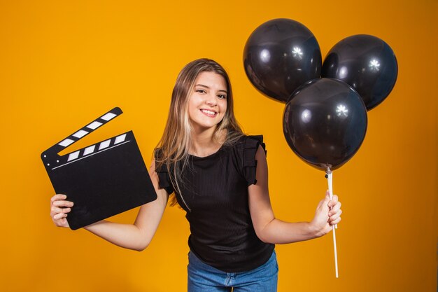 Young woman holding an audio-visual clapper board and black balloons during Black Friday. Promotion concept. Black Friday