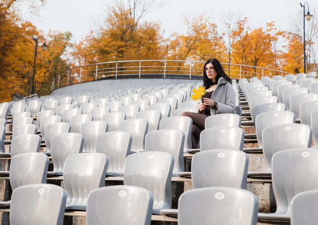 Foto giovane donna con una foglia d'autunno seduta allo stadio