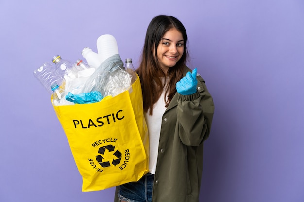 リサイクルするペットボトルの完全な袋を保持している若い女性