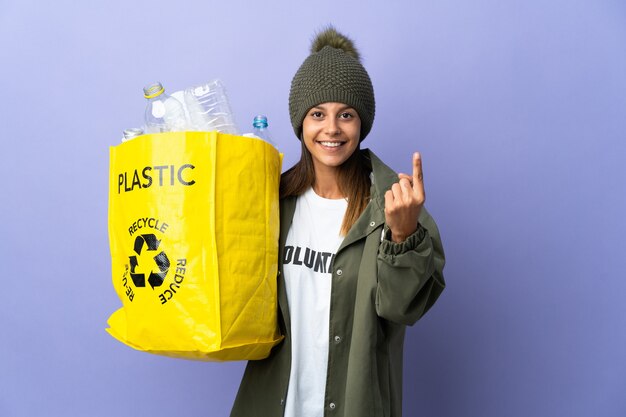 Young woman holding a bag full of plastic doing coming gesture