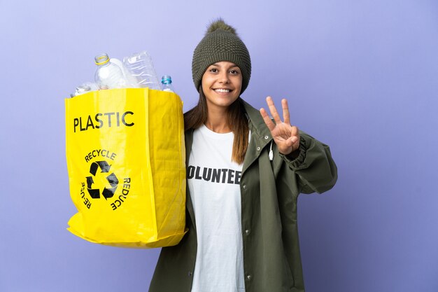 幸せなプラスチックでいっぱいのバッグを持って、指で3を数える若い女性