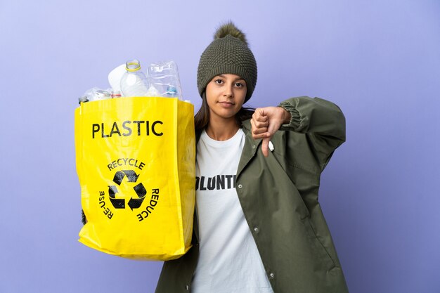 Young woman holding a bag full of plastic showing thumb down with negative expression