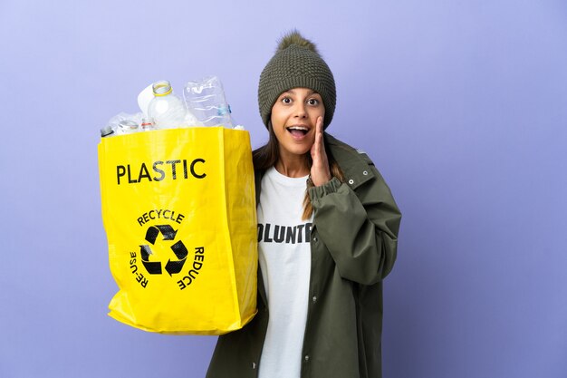 Giovane donna che tiene un sacchetto pieno di plastica con espressione facciale sorpresa e scioccata