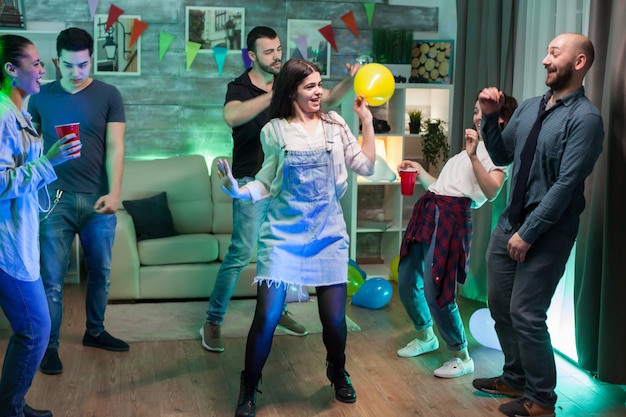 Молодая женщина, держащая воздушный шар с гелием, танцуя на вечеринке со своими друзьями.