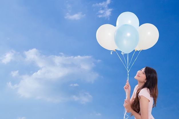 Young woman holding balloons on sky background