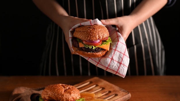 Young woman holding beef burgers with napkin in restaurant with black wall