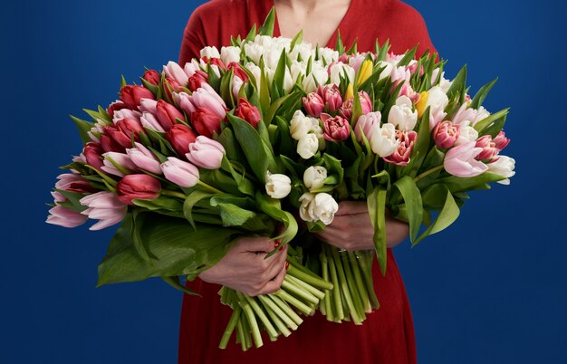 young woman holding the big bouquet of colorful tulips over blue 