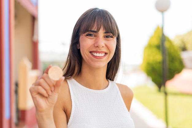 幸せそうな表情で屋外で Bitcoin を保持している若い女性