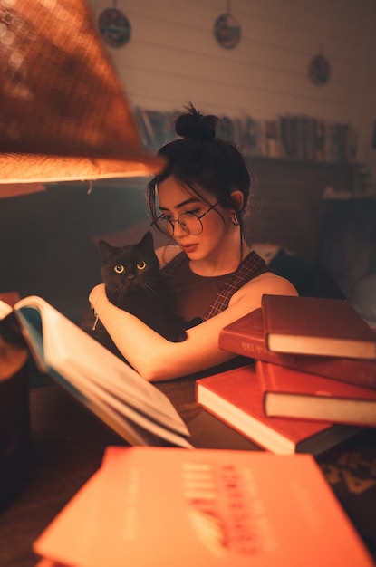 Young woman holding black cat and reading