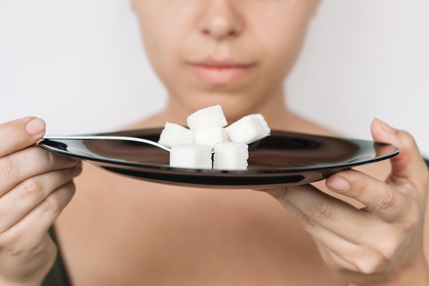 Foto giovane donna con un piatto nero e un cucchiaio con cubetti di zucchero raffinato dipendenza da zucchero bianco