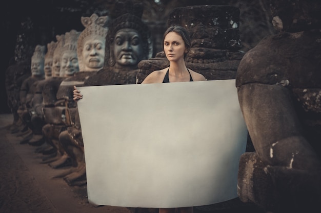 Young woman holding blank placard in dark mystic location