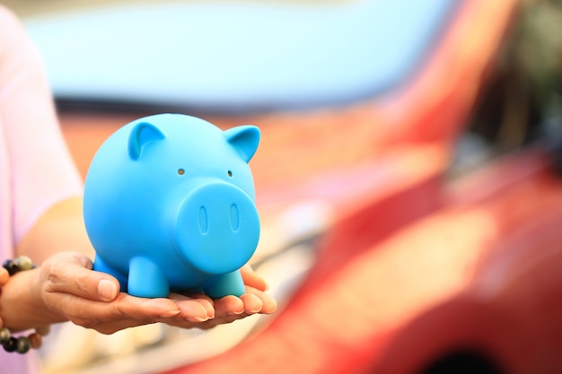 Young woman holding blue piggy with standing at the car parking 