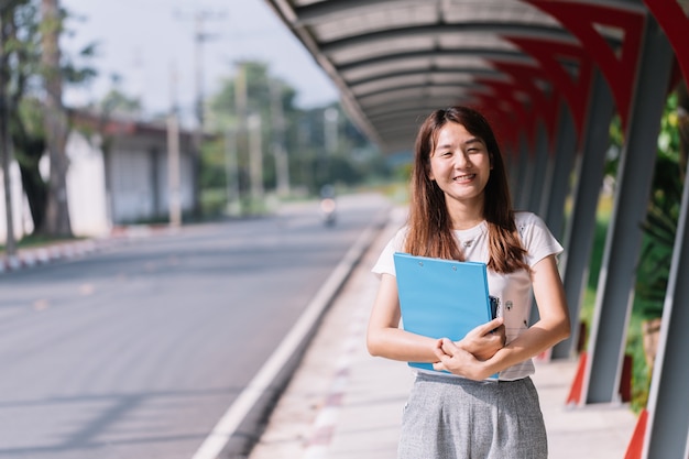 キャンパスで幸せに笑いながら本を持っている若い女性。