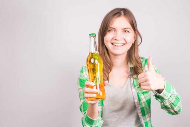 Young woman holding bottle of beer and showing thumbs up gesture.