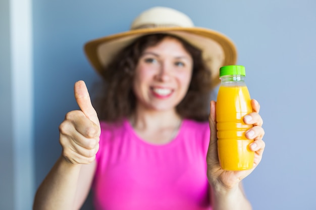 Young woman holding a bottle with juice and showing thumbs up gesture