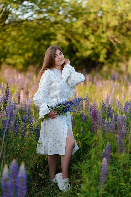 Photo a young woman holding a bouquet of lupins in a field