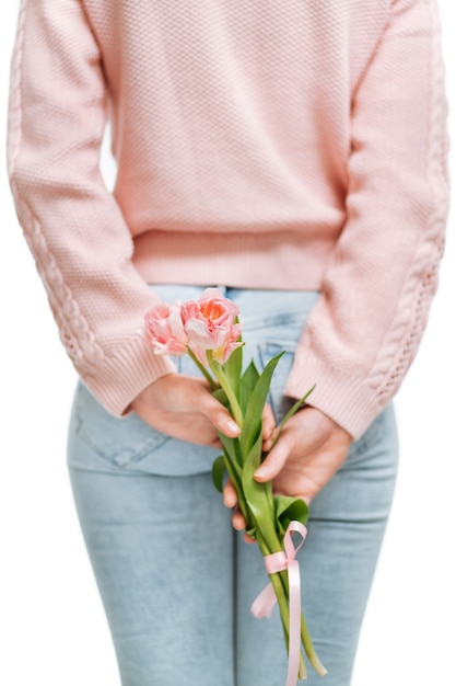 흰색 배경에 등 뒤에서 분홍색 튤립 꽃다발을 들고 있는 젊은 여성. 텍스트 공간, 선택적 초점.