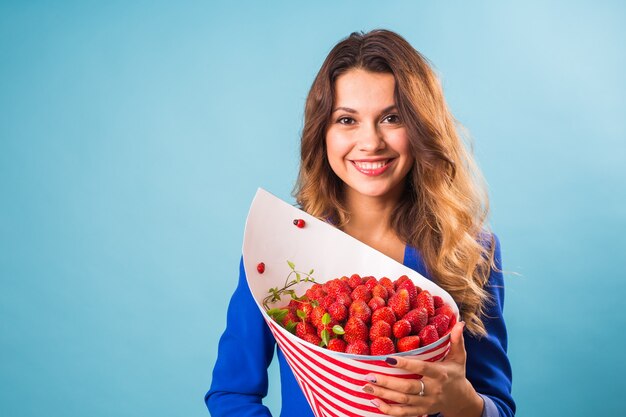 Young woman holding bouquet of strawberries on blue background.