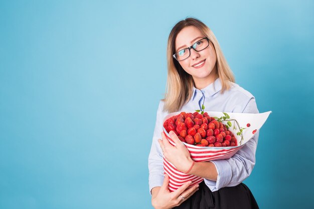 Young woman holding bouquet of strawberries on blue\
background