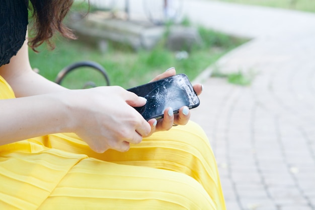 Young woman holding broken phone in the park