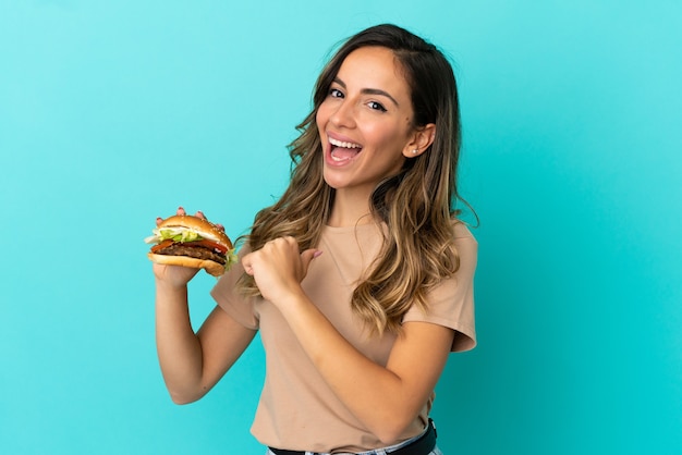 Young woman holding a burger over isolated background proud and self-satisfied