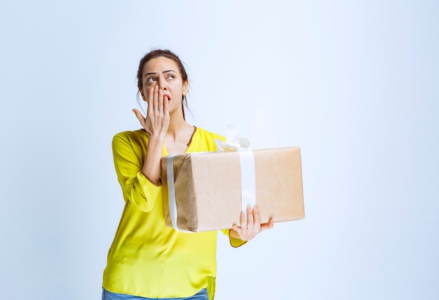 Young woman holding a cardboard gift box and thinking about the unknown sender