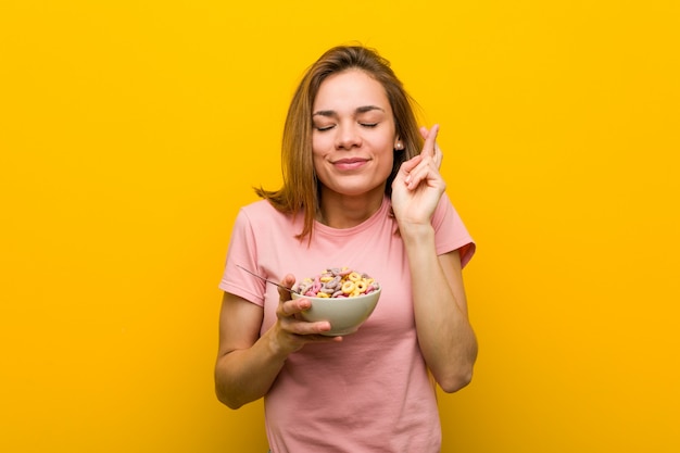 Young woman holding a cereals bowl crossing fingers for having luck