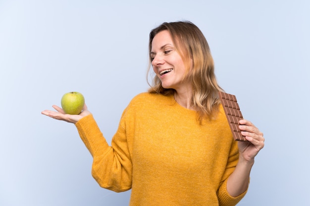 Young woman holding chocolate and an apple
