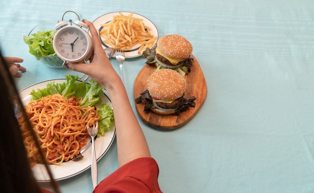 時計を保持し、朝食を食べる準備ができて若い女性