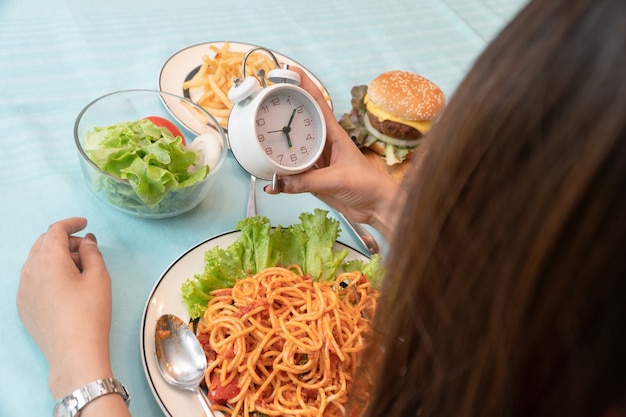 時計を保持し、夕食を食べる準備ができて若い女性