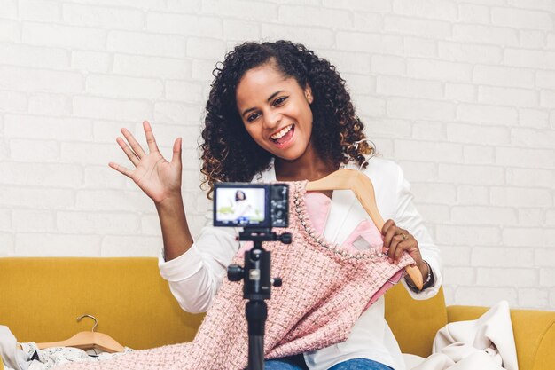 Photo young woman holding cloth while recording on camera against wall