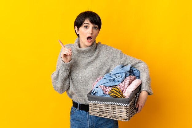 Young woman holding a clothes basket intending to realizes the solution while lifting a finger up