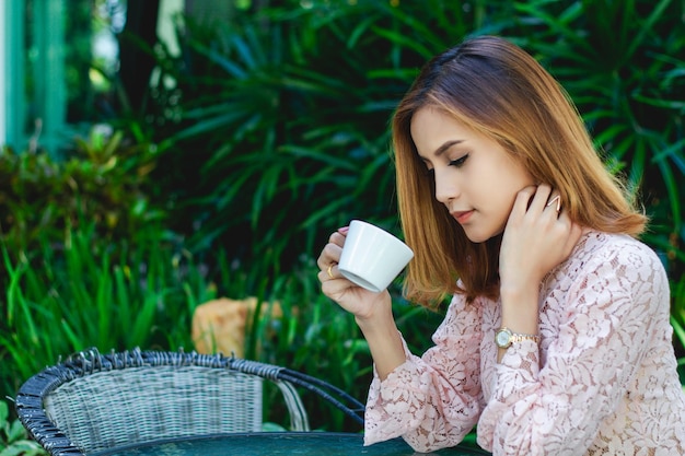 カフェのテーブルに座っている若い女性がコーヒーカップを握っている