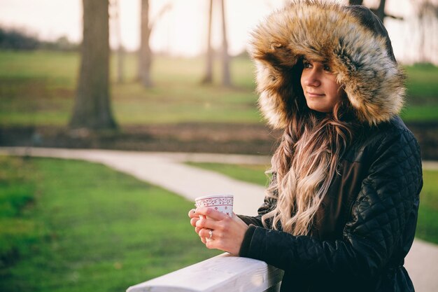 Photo young woman holding coffee cup while wearing warm clothes