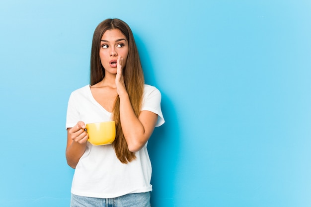 Young woman holding a coffee mug is saying a secret hot braking news and looking aside