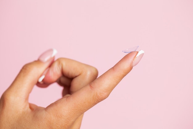 Young woman holding contact lens on finger.