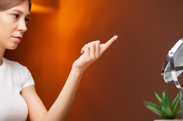 Young woman holding contact lens on finger.