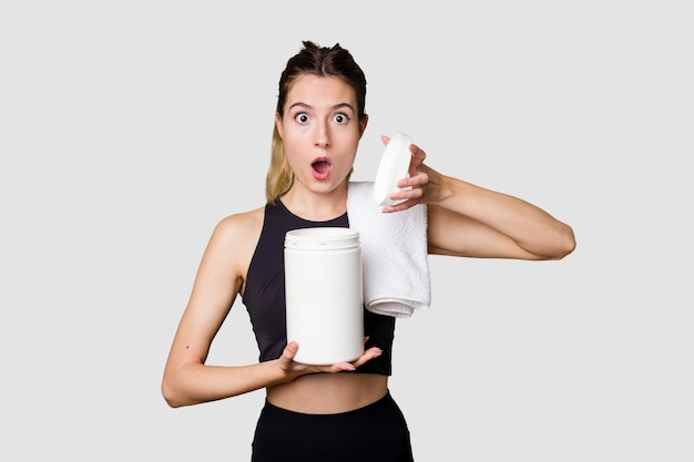 Young woman holding a container of protein powder dressed in sportswear