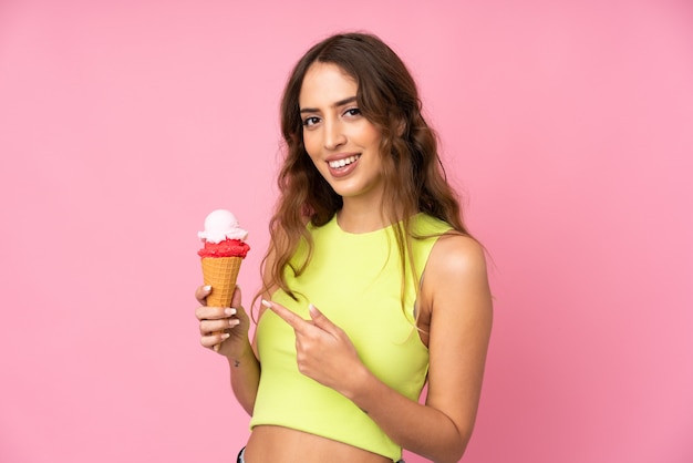 Молодая женщина держит мороженое корнет над изолированные на розовой стене и указывая его