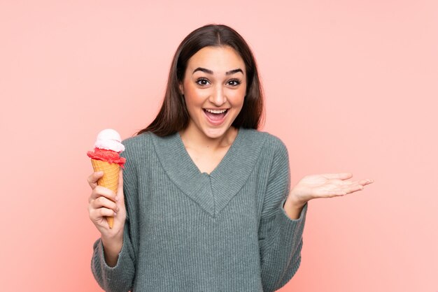 Young woman holding a cornet ice cream isolated on pink wall with shocked facial expression